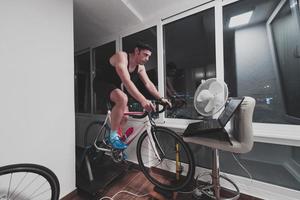 homem andando de bicicleta no treinador de máquina ele está se exercitando em casa à noite jogando jogo de corrida de bicicleta online foto