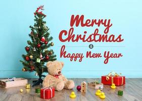 árvore de natal, bandeira e decorações de natal com ursinho de pelúcia de brinquedo em fundo azul, com redação feliz natal e feliz ano novo foto
