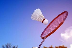 raquete de badminton e peteca de badminton contra fundo nublado e azul, conceito de jogo de badminton ao ar livre. foco seletivo na raquete. foto