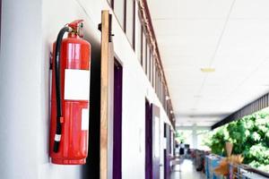 um extintor de incêndio vermelho é instalado em uma parede de cimento branco na varanda da frente do prédio para ser usado para extinguir um incêndio em caso de incêndio no prédio. foto
