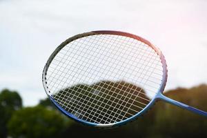 raquete de badminton e peteca de badminton contra fundo nublado e azul, conceito de jogo de badminton ao ar livre. foco seletivo na raquete. foto