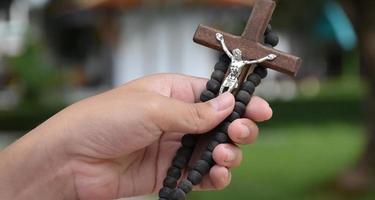 cruz de madeira e rosário de madeira são mantidos nas mãos da jovem oração católica asiática enquanto reza na área do parque do templo. foto