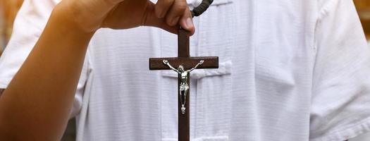 cruz de madeira e rosário de madeira são mantidos nas mãos da jovem oração católica asiática enquanto reza na área do parque do templo. foto