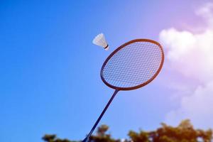 raquete de badminton e peteca de badminton contra fundo nublado e azul, conceito de jogo de badminton ao ar livre. foco seletivo na raquete. foto