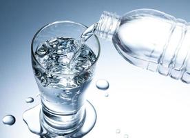 derramando água pura fresca da garrafa em um copo sobre a mesa com gotas de água, conceito de hidratação de saúde e beleza foto