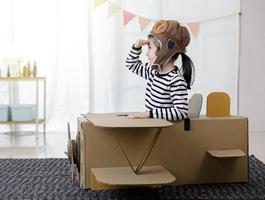 menina criança asiática brincando com artesanato de avião de brinquedo de papelão isolado em casa com espaço de cópia para o seu texto, criativo com a família e sonhando com o conceito de voar foto