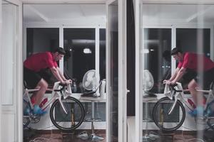 homem andando de bicicleta no treinador de máquina ele está se exercitando em casa à noite jogando jogo de corrida de bicicleta online foto