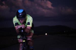 atleta de triatlo andando de bicicleta rápido à noite foto