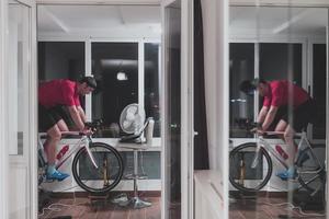 homem andando de bicicleta no treinador de máquina ele está se exercitando em casa à noite jogando jogo de corrida de bicicleta online foto