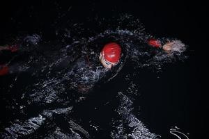 atleta de triatlo nadando na noite escura vestindo roupa de mergulho foto