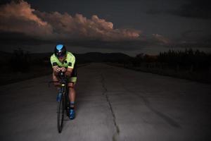 atleta de triatlo andando de bicicleta rápido à noite foto