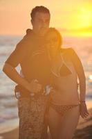 casal de surf posando na praia ao pôr do sol foto