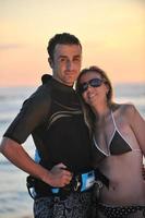casal de surf posando na praia ao pôr do sol foto