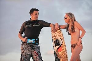 casal de surf posando na praia ao pôr do sol foto