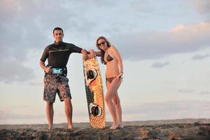 casal de surf posando na praia ao pôr do sol foto