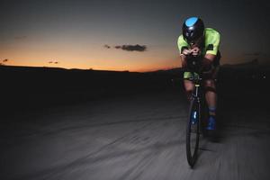 atleta de triatlo andando de bicicleta rápido à noite foto