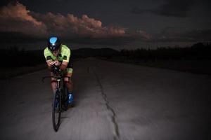 atleta de triatlo andando de bicicleta rápido à noite foto