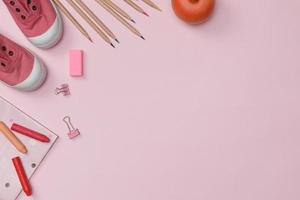 flatlay criativo de mesa rosa de educação com livros estudantis, sapatos, giz de cera colorido, espaço vazio isolado no fundo rosa, conceito de educação e volta às aulas foto