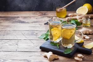 duas xícaras de chá de ervas naturais gengibre limão hortelã e mel em um fundo de madeira. espaço de cópia