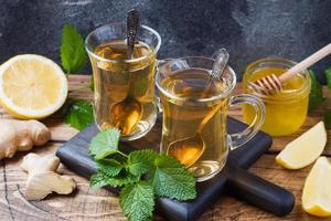 duas xícaras de chá de ervas naturais gengibre limão hortelã e mel em um fundo de madeira. foto