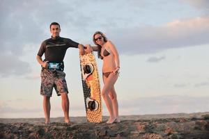 casal de surf posando na praia ao pôr do sol foto
