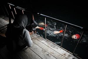 cinegrafista tomando uma foto de ação do atleta de natação de triatlo à noite