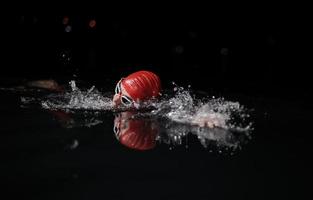 atleta de triatlo nadando na noite escura vestindo roupa de mergulho foto