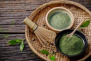 pó de chá verde matcha orgânico japonês em tigela com batedor de arame e folha de chá verde em fundo de madeira, produto orgânico da natureza para saudável com estilo tradicional foto