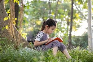 uma menina muito asiática lendo um livro debaixo da grande árvore. foto