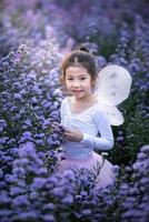 menina sorridente bonitinha usa uma fantasia de fada de balé mágico em lindo roxo do campo de flores de margaret. foto