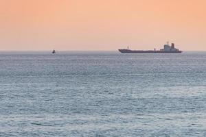 pequeno rebocador e grande cargueiro. belo pôr do sol sobre o mar. vista de viagem de tirar o fôlego, copie o espaço. foto