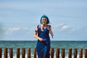 artista performática artística mulher de cabelos azuis manchada com tintas guache azul dançando na praia foto