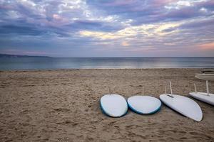 algumas pranchas de surf na praia à beira-mar na hora do pôr do sol com belas nuvens. fundo de esportes aquáticos foto