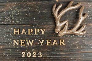 feliz ano novo 2023 citação feita de letras de madeira e chifres de rena dourada como decoração. cartão festivo para feriados de natal e ano novo foto