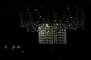 lustre de cristal feito de vidro. candelabro no interior. luz no escuro. reflexo da luz no vidro. foto
