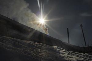fumaça da chaminé no fundo do sol. raios brilhantes no céu. vista de fumaça. foto