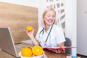 nutricionista sorridente em seu escritório, ela está segurando uma fruta e mostrando vegetais e frutas saudáveis, conceito de saúde e dieta. nutricionista feminina com frutas trabalhando em sua mesa foto