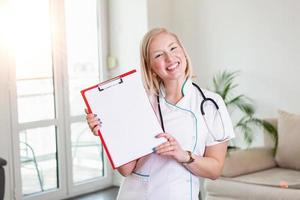 feliz médico segurando vazio em branco nas mãos. médica mostrando uma prancheta com papel em branco. close-up de uma médica com jaleco e segurando a área de transferência em branco foto