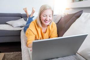 jovem albina fazendo trabalho de pesquisa para seu negócio. mulher sorridente sentada no sofá enquanto navega no site de compras online. garota feliz navegando pela internet durante o tempo livre em casa. foto