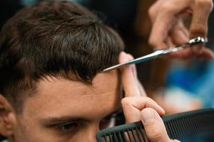 barbearia. close-up do corte de cabelo do homem, mestre faz o penteado na barbearia. close-up, o mestre barbeiro faz o penteado e o estilo com uma tesoura. barbearia conceito. foto