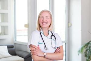 médico confiante de braços cruzados. médico jovem sorridente confiante. médico estagiário jovem mulher bonita em roupas brancas com um estetoscópio posando e sorrindo. foto