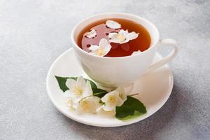 xícara de chá com flores de jasmim em uma mesa cinza com espaço de cópia. foto