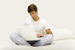 homem sentado na cama usando laptop foto