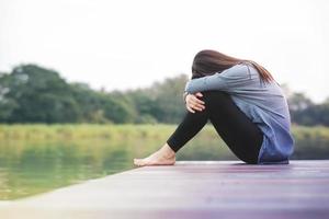 conceito de dia ruim. mulher de tristeza sentada à beira do rio no deck de madeira do pátio. sem rosto com corpo inteiro, vista lateral foto