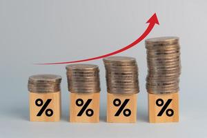 negócios finanças investimentos economia pilha moeda inflação e seta vermelha com porcentagem de cubo de madeira na mesa. foto