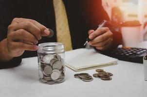 mão de homem colocando moedas de dinheiro e anote as receitas e despesas e trabalhando para economizar dinheiro para o futuro crescimento dos negócios, educação e aposentadoria. foto