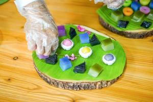 a mão do chef tailandês está decorando variedades de sobremesas tailandesas coloridas tradicionais conjunto de farinha fumegante, creme preto, creme de coco, feijão fumegante, bolo de pudim de camada foto