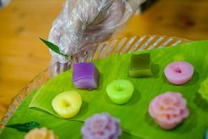 a mão do chef tailandês está decorando variedades de sobremesas tailandesas coloridas tradicionais conjunto de farinha fumegante, creme preto, creme de coco, feijão fumegante, bolo de pudim de camada foto