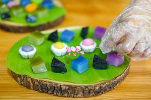 a mão do chef tailandês está decorando variedades de sobremesas tailandesas coloridas tradicionais conjunto de farinha fumegante, creme preto, creme de coco, feijão fumegante, bolo de pudim de camada foto