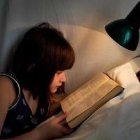 menina ler livro na cama à noite foto